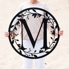 a woman holding up a sign with the letter m in it's center and leaves