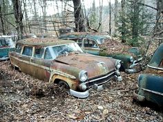 an old rusted out car sitting in the woods