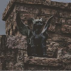 a gargoyle statue sitting on top of a stone wall