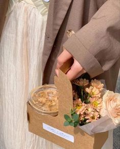 a person holding a box with flowers in it and a jar filled with something next to it