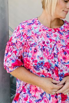 Get ready to bloom in the Harley Top! This playful pink top is adorned with pink and blue flowers, adding a touch of whimsy to any outfit. With a convenient button up design and banded sleeves, this top is both stylish and comfortable. The ruffle across the bodice and sleeves adds a feminine touch. Fits true to size. Model is wearing a 1X and is 5'7". Size Chart Length Bust 1x 25" 50" 2x 26" 52" 3x 27" 54" *All measurements are approximate and done while hanging.* Fabric and Care 85% Rayon 15% N Pink Ruffle Sleeve Tops For Summer, Floral Print Ruffle Sleeve Blouse For Vacation, Casual Ruffled Blouse For Garden Party, Pink Feminine Blouse For Vacation, Feminine Pink Blouse For Vacation, Casual Pink Spring Blouse, Spring Ruffle Sleeve Tops For Garden Party, Ruffle Sleeve Tops For Spring Garden Party, Casual Pink Blouse For Spring