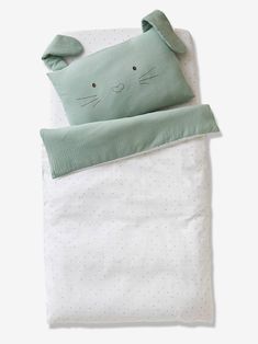 a green cat pillow on top of a white bed with polka dot sheets and pillows