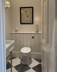 a white toilet sitting inside of a bathroom next to a sink under a framed painting