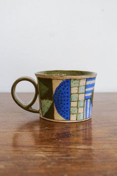 a coffee cup with blue and green designs on it sitting on a wooden table next to a white wall