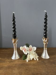 three metal candlesticks with flowers on a wooden table next to eachother