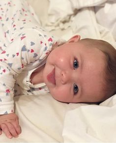 a smiling baby laying on top of a bed