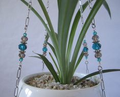 a potted plant with blue beads and chains hanging from it's side, next to a white wall