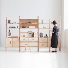 a woman standing in front of a wooden shelf with shelves and drawers on top of it