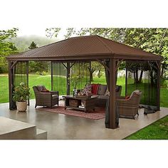 a gazebo sitting on top of a patio next to a lush green field and trees