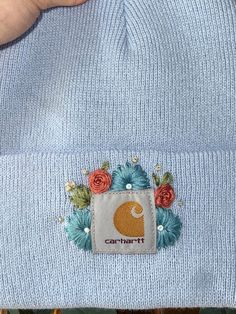 someone wearing a blue beanie with flowers on the front and an applique