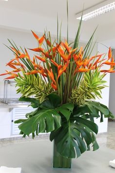 a vase filled with orange flowers on top of a white countertop next to a green leafy plant