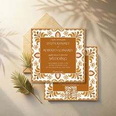 an orange and white wedding card on top of a brown envelope next to a palm tree