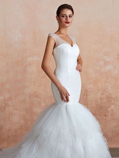 a woman in a white wedding dress standing next to a pink wall and posing for the camera