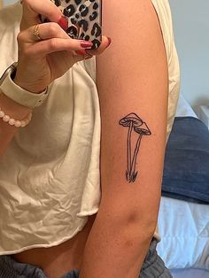 a woman is taking a selfie with her cell phone and mushroom tattoo on her arm