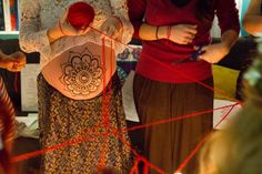 two women standing next to each other with red yarn on their stomachs and hands