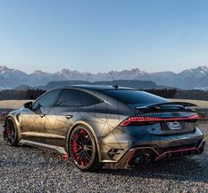 the rear end of a silver sports car parked on gravel with mountains in the background