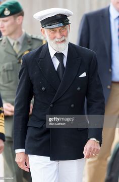 an older man wearing a suit and hat walks with other men in uniform behind him