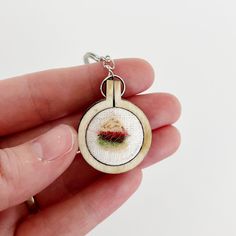 a hand holding a needle - embroidered keychain with a red flower on it