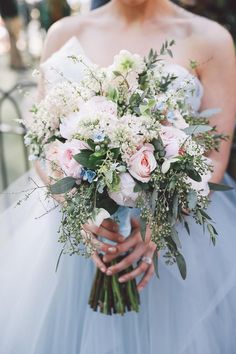 a bride holding a bouquet of white and pink flowers with greenery in her hands