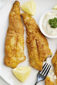 fried fish on a white plate with lemon wedges and sour cream sauce next to it