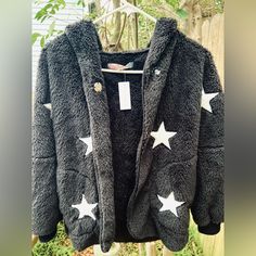 This Is A Black, Fuzzy Fabric Hoodie With Star Details And A Button Clasp Sold By A Local Brand; Lemondrop (Which Is No Longer In-Store) And Vintage Havana. This Jacket Is New With The Tag Still On, Originally Priced At $65. This Is A Children’s Jacket In A Size Large, The Full Length Being ~35-36in (Measured From Top Of The Hood To The Bottom Of The Jacket) || The Fabric Of This Jacket Is Very Soft, Cozy, And Provides Some Stretch. It Has Pockets And Cuffs At The End Of The Sleeves. Black Long Sleeve Outerwear With Star Print, Black Star Print Winter Outerwear, Black Star Print Outerwear For Winter, Cute Fall Hoodie Outerwear, Cute Hoodie Outerwear For Fall, Trendy Winter Outerwear With Star Print, Cute Black Winter Outerwear, Cute Black Outerwear For Winter, Cute Black Hooded Outerwear