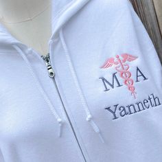 a white hoodie with an embroidered medical symbol on the chest and name, m a yneh