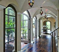 an arched entry way with wood floors and glass doors leading to another room that has potted plants on the other side