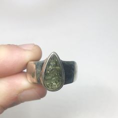 This genuine moldavite ring weighs 7.6 grams and is a size US 7.5. This rare stone sits in all sterling silver, the front is faceted and the back is raw. Our Moldavite is guaranteed 100% genuine from the Czech Republic. Moldavite comes from a meteor collision with Earth almost 15 million years ago. Found only in the Czech Republic these green Gems are one of the most rare minerals on Earth. This tektite is composed of natural glass and is created when a meteorite collides with earth resulting in Green Teardrop Polished Jewelry, Sterling Silver Teardrop Rings, Teardrop Ring With Natural Inclusions For Gift, Untreated Teardrop Silver Ring, Green Teardrop Jewelry With Bezel Setting, Unique Untreated Teardrop Rings, Handmade Teardrop Ring For Anniversary, Rare Minerals, Moldavite Ring