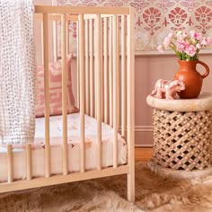 a baby's crib with pink flowers in a vase on the end table