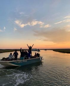 a group of people riding on top of a boat in the water at sunset with their arms up