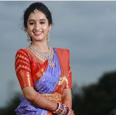 a woman in an orange and blue sari smiles at the camera with her arms crossed