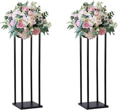 two tall black vases with flowers and greenery on them, one is standing upright