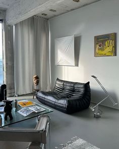 a living room filled with furniture next to a large window and a painting on the wall