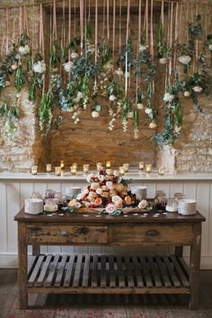 a wooden table topped with lots of cupcakes next to a wall covered in greenery