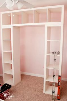 a room with pink walls and a white bookcase in the corner, next to a ceiling fan