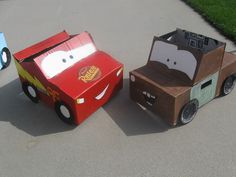 three cardboard cars are sitting on the ground in front of each other, one is red and one is blue