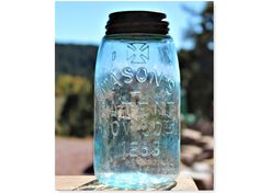 a blue mason jar sitting on top of a wooden table next to some rocks and trees