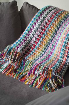 a multicolored blanket sitting on top of a gray couch next to a pillow