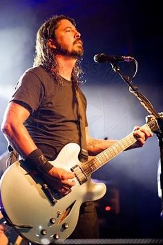 a man with long hair playing an electric guitar in front of a microphone on stage