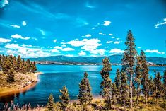 a lake surrounded by trees and mountains under a blue sky with clouds in the background