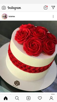 a white and red cake with roses on the top sitting on a table in front of an instagram page