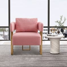 a pink chair sitting in front of a window next to a table with a vase on it