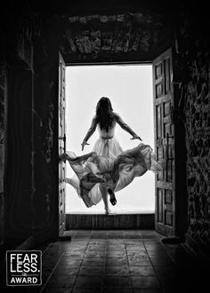 a woman in a long dress is jumping into an open door with her arms outstretched