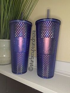 two blue cups sitting on top of a white shelf next to a potted plant