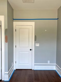 an empty room with white doors and blue tape on the wall behind it is a wood floor