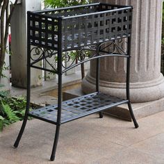 a black metal bench sitting next to a tall stone pillar and planter in front of a building