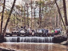 a group of people standing around four wheelers in the woods