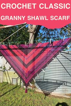 the crochet triangle shawl is hanging from a tree in front of a metal tank