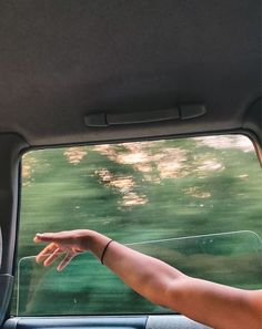 a person's hand reaching out the window of a car with trees in the background