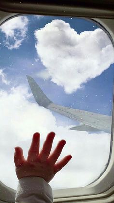 a person's hand reaching out the window of an airplane as it flies in the sky